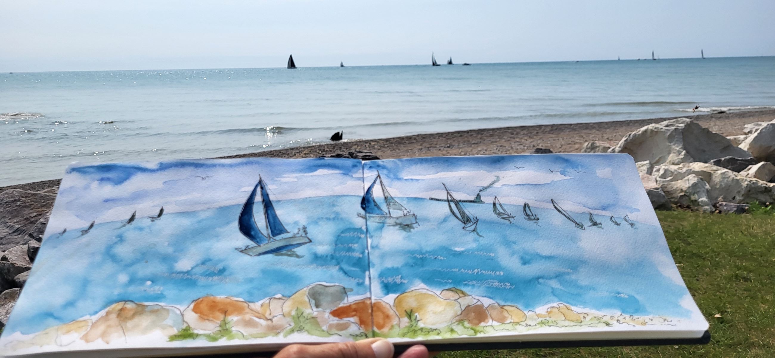 Watercolor drawing of sailboats on water is displayed on a Lake Michigan beach